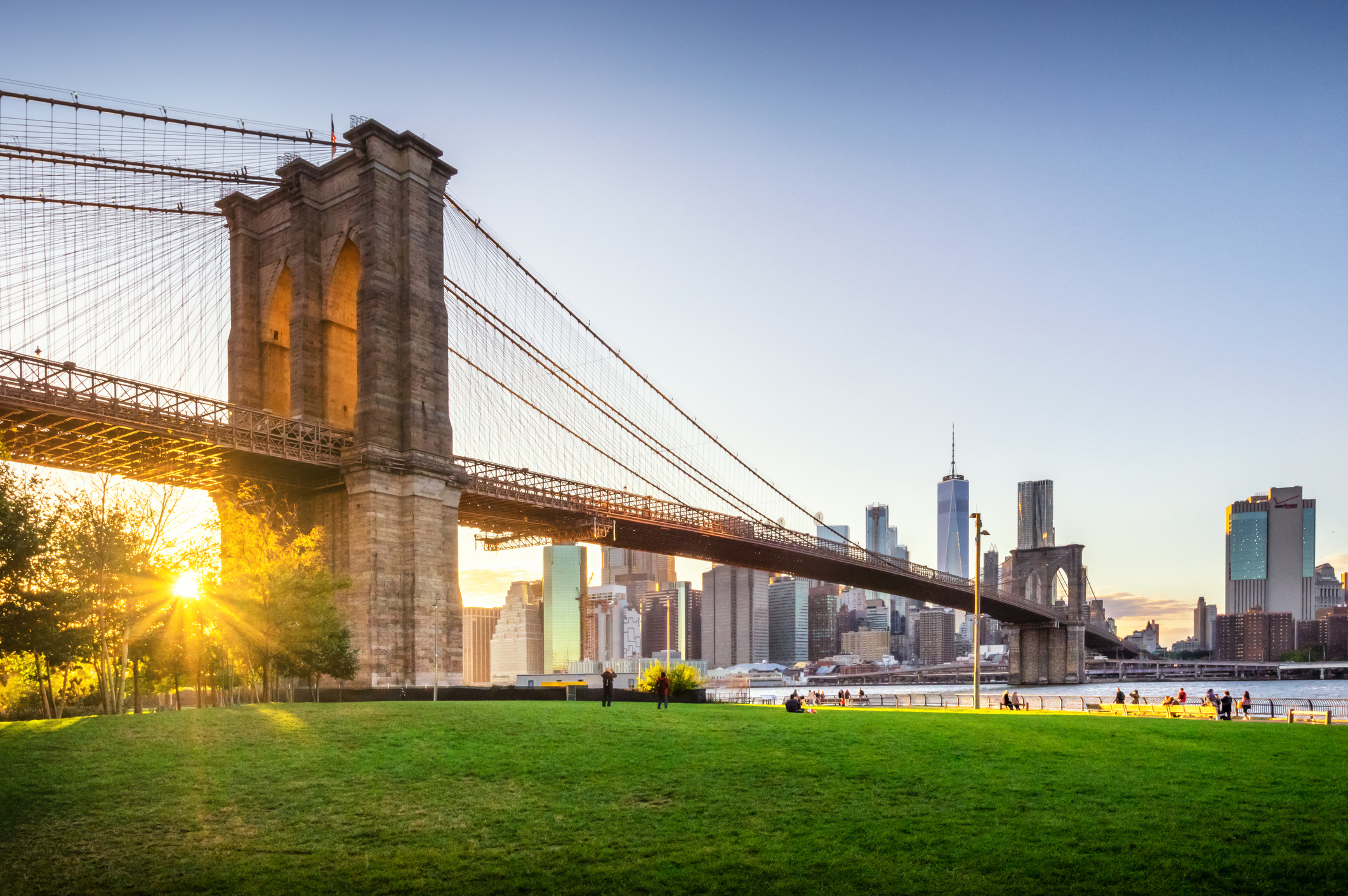Brooklyn Bridge and Manhattan skyline at sunset with people relaxing in the park